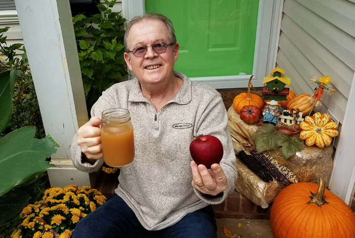 Wayne holding a glass of apple juice and a delicious apple on our front porch.